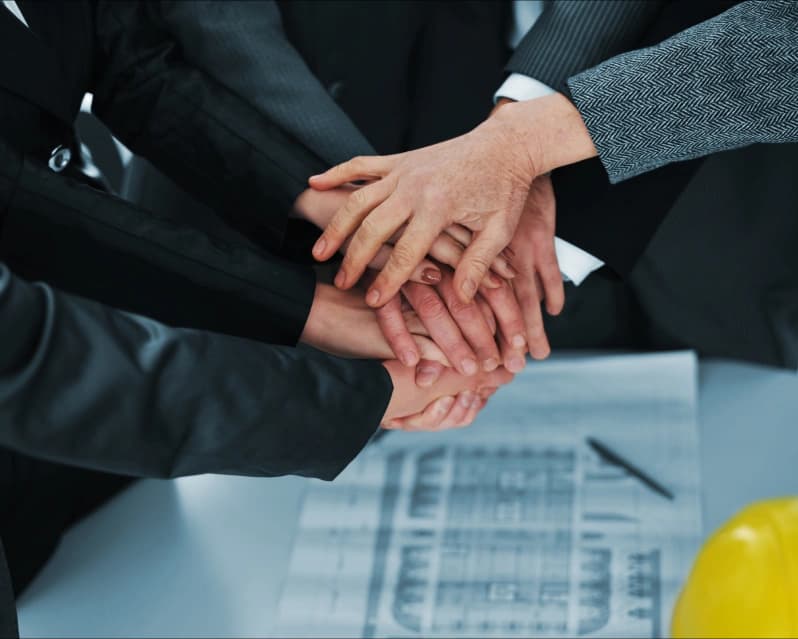 Business team hands together over blueprints in a collaborative huddle